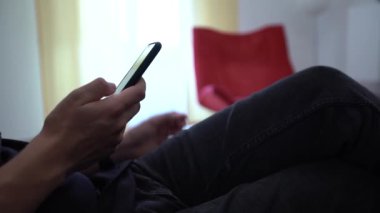 4K, beyaz adam akıllı telefon kullanıyor, evdeki kanepede oturuyor. Erkek el, evin içinde cep telefonuna dokunuyor. İnternette sörf yapmak, sosyal ağı kontrol etmek ve mobil Dan aygıtına metin yazmak