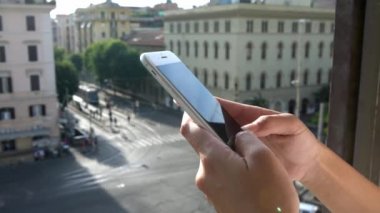 4K, kız turist pencerede duruyor ve internette gezinmek için cep telefonu kullanıyor ve sosyal ağları kontrol ediyor. Gündüz vakti Roma şehrindeki bir binanın tepesinden sokaktaki insanların görüntüsü yükseliyor.