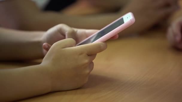 Closeup若い学生が電話でテキストを読んでいます 教室の木製の机の上にスマートフォンの画面を探している子供たち 10代の手の情報を検索するスマートフォンを保持 教育理念 — ストック動画