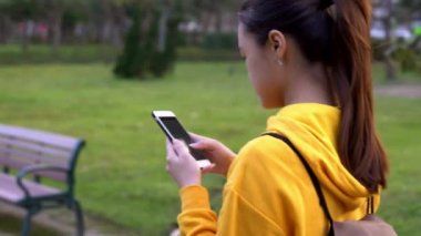4K, Mutlu Asyalı kadın parkta yürüyüş yapıyor ve Taipei 'de akıllı telefon kullanıyor. İnternette sörf yapmak için kullanılan telefon aygıtını kullanan kız gülümsemesi, güzel Tayvan bahçe Dan 'indeki sosyal ağları kontrol ediyor