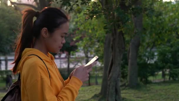 4Kハッピーアジアの女性が公園を散歩し 台北でスマートフォンを使用しています 女の子の笑顔は インターネットをサーフィンするために使用される携帯電話のデバイスながら 美しい台湾の庭でソーシャルネットワークをチェックダン — ストック動画