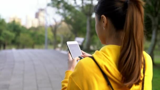 アジアの女性は公園を散歩し 台北でスマートフォンを使用しています 女の子の観光旅行やインターネットサーフィンのための携帯電話のデバイスを使用し ソーシャルネットワークをチェックし 台湾の庭でテキストを書き込みます — ストック動画