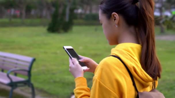 幸せなアジアの女性が公園を散歩し 台北でスマートフォンを使用しています 女の子の笑顔は インターネットをサーフィンするために使用される携帯電話のデバイスながら 美しい台湾の庭でソーシャルネットワークをチェックダン — ストック動画