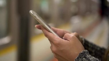 4K, genç bayan metro istasyonunda akıllı telefondan el ele tutuşun. İnternette sörf yapmak için telefon kullanan Asyalı bir kız, sosyal ağlara bak ve resimlere bak. Osaka tren istasyonu platformu. Japonya-Dan