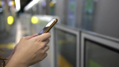 4K Genç Asyalı kadın aktif metro platformunda akıllı telefon kullanıyor. Tren geçerken, kız sosyal ağları kontrol eder ve Tokyo tren istasyonu Japonya-Dan platformuna yapılan metinleri yazar.