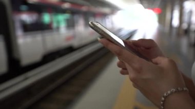 4K Genç Asyalı kadın aktif metro platformunda akıllı telefon kullanıyor. Tren geçerken, kız sosyal ağları kontrol eder ve Kuala Lumpur tren istasyonundaki telefon cihazına mesaj yazar. Malezya - Dan