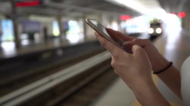 4K Genç Asyalı kadın aktif metro platformunda akıllı telefon kullanıyor. Tren geçerken, kız sosyal ağları kontrol eder ve Kuala Lumpur tren istasyonundaki telefon cihazına mesaj yazar. Malezya - Dan