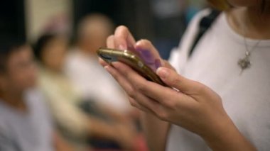 Trendeki 4K Asyalı genç kadın telefonunu kontrol ediyor ve arkadaşlarıyla mesajlaşırken hat, sosyal ağ kullanıyor, Tayvan-Dan durağına varmasını bekliyor.