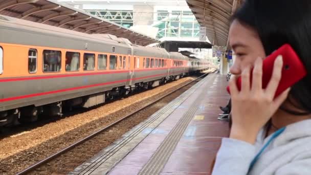 列車が通過すると 台湾の駅のプラットフォーム上で彼女のモバイルデバイスと話す女性 — ストック動画