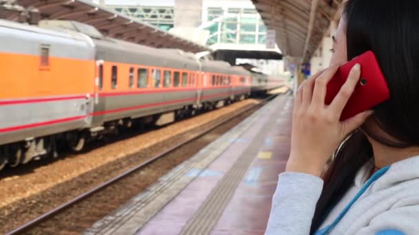 列車が通過すると 台湾の駅のプラットフォーム上で彼女のモバイルデバイスと話す女性 — ストック動画