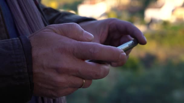 4K Gros plan d'homme caucasien mains utilisant un téléphone portable à écran tactile le jour dans le fond du parc de la ville. Surfer sur Internet, vérifier les réseaux sociaux et écrire du texte sur smartphone Dan 