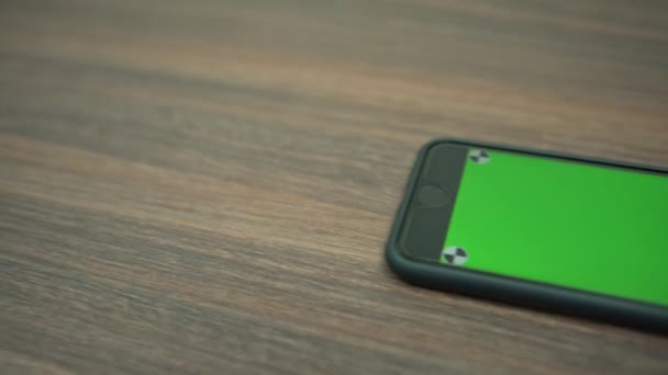 4K Gros plan du téléphone à écran vert. Smartphone sur la table en bois d'un bureau d'affaires. Utilisation du téléphone intelligent avec clé chromatique pour une publicité.-Dan 