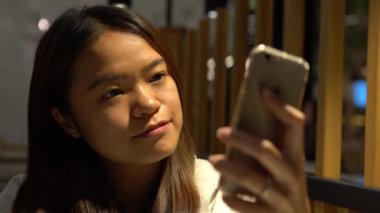 4K Gülümseyen Mutlu Asyalı Kadın Restoranda Beklemek, telefon cihazında bazı işleri halletmek için iyi bir zaman, akıllı telefonu e-postalarını ve yazışmalarını kontrol etmek için kullanmak, o beklerken - Dan