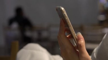 4K Close Up of Asian Woman Hand Mobil Dokunmatik Cep Telefonu Kullanıyor Restoranın İçinde İnsanlar Oturuyor. İnternette sörf yapmak, sosyal ağı kontrol etmek ve akıllı telefondan Dan 'e metin yazmak.