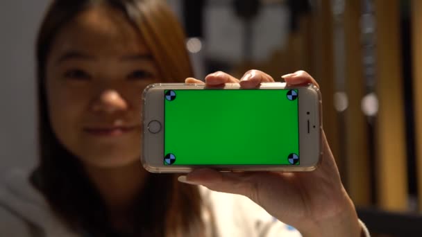 4K微笑快乐的女人在餐厅里展示绿色屏幕电话 漂亮的亚洲女孩拿着智能手机 用在一个广告上 — 图库视频影像