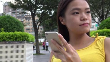 Asyalı genç bir kadın sokakta durup telefonunu kontrol ediyor ve arkadaşlarıyla SMS mesajları yazıyor. Line, sosyal ağ kullanıyor. Küçük bir gülümseme, Tayvan-Dan sokağı.