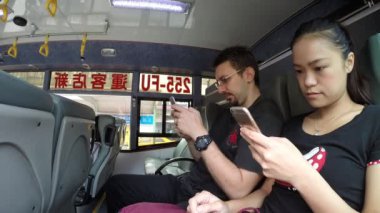 Asyalı kadın ve beyaz adam otobüs Taipei 'de akıllı telefon aygıtı kullanıyor. Telefon cihazını tamir etmek için iyi bir zaman. Akıllı telefonu Cheks e-postaları ve yazı yazma metinleri için kullanıyorlar.
