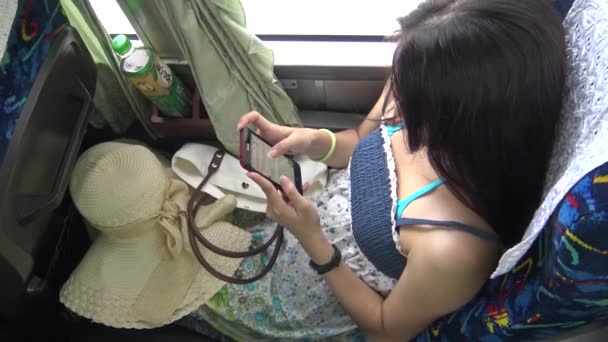 アジアの女性は タッチスクリーンタブレットスマートフォンデバイスを使用しました 若い女性は タッチパッド上のビデオを見て その後 バス内で一日乗車中に別のものを選択 Dan — ストック動画