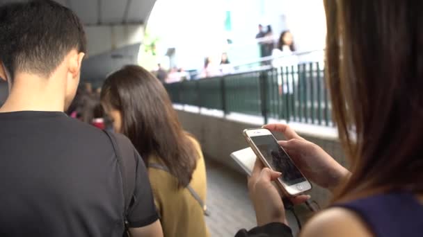4K香港のビクトリアピークに向かってトラムに乗るために長い列にスマートフォンを使用して観光客の群衆 夜のラッシュ時には有名な観光名所 人々は電話ダンをチェック — ストック動画