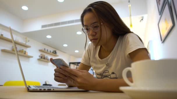 4Kアジアの女性は コーヒーショップで何かを読むためにスマートフォンやノートパソコンを使用しています チャットや連絡先の人々にインターネットやタッチスクリーンをサーフィン 彼女のノートブックダン上のソーシャルネットワークや電子メールをチェック — ストック動画