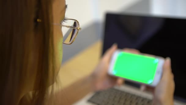 Close アジアの女性の手は コーヒーショップのテーブルの中に1台のコンピュータの背景を持つグリーンスクリーン電話を示しています 1つの広告のためのスマートフォンの使用 — ストック動画