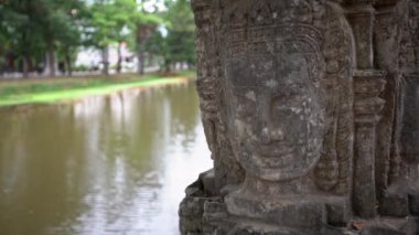 4K, Kamboçya 'nın Siem Reap kentindeki şehir merkezinde gülen yüzlü taş heykel. Şehir merkezindeki parkın yanındaki nehrin yanındaki antik heykeller. Konsept simgesi ve seyahat - Dan