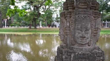 4K, Kamboçya 'nın Siem Reap kentindeki şehir merkezinde gülen yüzlü taş heykel. Şehir merkezindeki parkın yanındaki nehrin yanındaki antik heykeller. Konsept simgesi ve seyahat - Dan