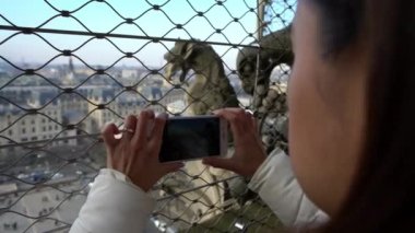 4K, turist kadın Paris 'in arka planındaki Notre Dame Katedrali' nde güzel bir heykelin fotoğrafını çekmek için akıllı telefon kullanıyor. İnsanlar tatilde kameralı telefonla fotoğraf çekiyor.