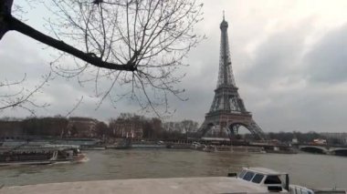 4K, Eyfel Kulesi ve Seine nehri. Paris, Fransa 'da bir kış gününün ağaç dallarının arkasında tekne. Avrupa 'nın ünlü turistik bölgelerinde ağaçlar ve bulutlu gökyüzü. Eiffel turuyla yağmurlu bir gün. Arka plan Dan.