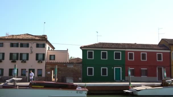 ブラーノ島の運河沿いのカラフルなヴェネツィアの家のファサードとボートの美しい景色 村のカラフルな塗装アパートの建物 ヴェネツィアのランドマークダン — ストック動画