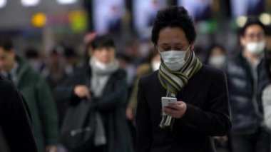 Tokyo, Japonya-04 Şubat 2020 Japon iş adamlarının yavaş çekimde yüz maskesi takması ve akıllı telefon kullanması. Koronavirüs sırasında önlem olarak maskeyi takan insanlar Wuhan, Çin-Dan 'den geliyor.