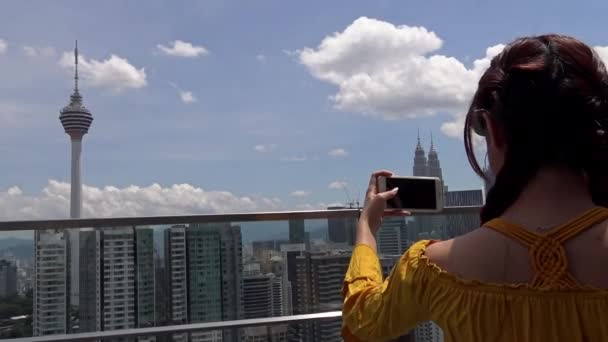 アジアの女性は有名なクアラルンプールの通信塔Menara Klのスマートフォンで写真を撮ります 観光客が訪問し アンテナを画像 マレーシア ダンのテレビ塔のスカイライン — ストック動画
