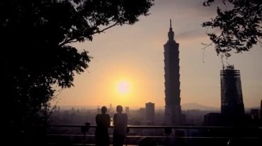 4K Silhouette, Tayvan-Dan 'da Taipei 101 binasının arka planında yer alan Taipei gökdeleniyle Fil Dağı' nda güzel bir gün batımı izleyen genç turist çifti.