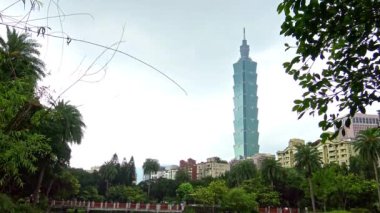 Tayvan 'ın Taipei 101. Kulesi' ndeki şehir suyuna yansıyan 4K yansıması. Yağmurlu bir günde Sun Yat Sen Memorial Hall 'dan yeşil ağaçlar ve palmiyeler. - Dan.