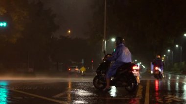 Taipei, Tayvan-29 Temmuz 2017: Taipei şehrinde Tayfun Nesat sırasında yağmurluk giyen bir adamın ağır çekimde kullandığı motosiklet. Geceleri şiddetli rüzgar ve yağmur. Tayvan-Dan 'de güçlü kasırga rüzgarları.