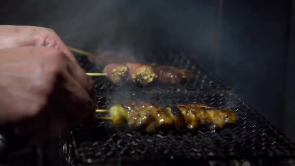 スローモーションベンダーは アジアのナイトマーケットストリートでスチールグリルで串焼きを調理します 人気の肉焼きBbqを作っています 木炭の炎 有名な市場だ おいしい日本料理団 — ストック動画