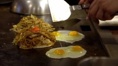 Yavaş çekim şefi Okonomiyaki Japon yemeği pişiriyor. İçinde çeşitli malzemeler, erişte, doğranmış lahana ve yumurta bulunan geleneksel krep. Monjayaki 'yi Japon-Dan restoranında kızartıyorlar.