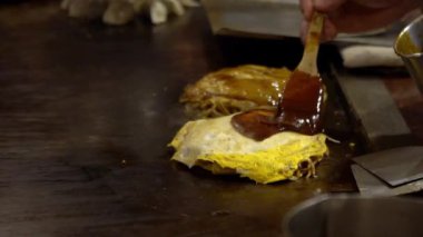 Yavaş çekim şefi Okonomiyaki Japon yemeği pişiriyor. İçinde çeşitli malzemeler, erişte, doğranmış lahana ve yumurta bulunan geleneksel krep. Monjayaki 'yi Japon-Dan restoranında kızartıyorlar.