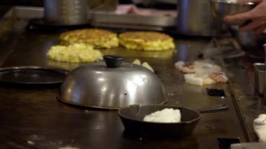 Yavaş çekim şefi Okonomiyaki Japon yemeği pişiriyor. İçinde çeşitli malzemeler, erişte, doğranmış lahana ve yumurta bulunan geleneksel krep. Monjayaki 'yi Japon-Dan restoranında kızartıyorlar.