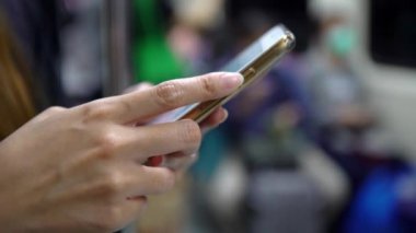 4K, Asyalı bir kadın metro istasyonuna varmayı beklerken akıllı telefon kullanıyor. Sosyal ağları kontrol eder ve telefon cihazında yapılan metinleri yazar. -Dan