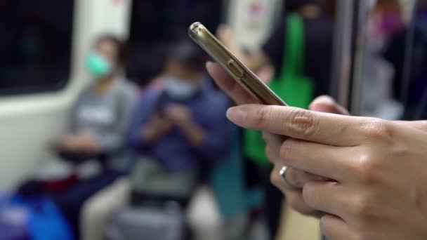 4K, femme asiatique utilisant un masque pour la protection du coronavirus et utilisant un smartphone dans le métro actif en attendant son arrivée à sa station d'arrêt. Vérifie les réseaux sociaux et d'écrire du texte fait sur l'appareil téléphone.-Dan 