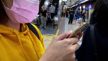 Taipei, Tayvan-07 Mart 2020: 4 K, Asyalı kadın akıllı telefon kullanıyor ve 2019-NCoV bulaşabilir enfeksiyonuna karşı maske takıyor. Wuhan, Çin 'de bulunan Coronavirus romanından. - Dan.