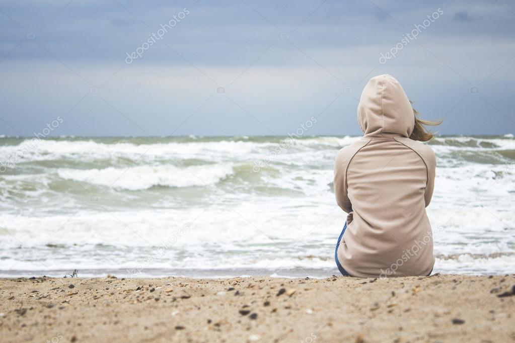 woman sitting alone on the shore of the stormy sea