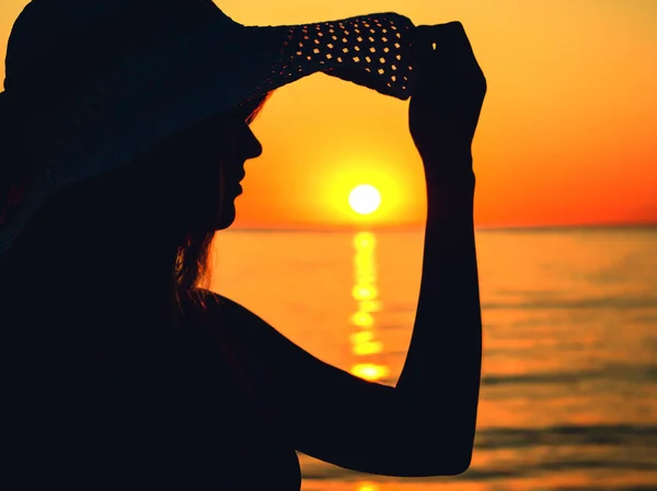 Silhueta de uma mulher em um chapéu de sol no mar ao amanhecer — Fotografia de Stock