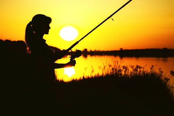 Silhouette di awoman con una canna da pesca sulla riva del fiume — Foto Stock