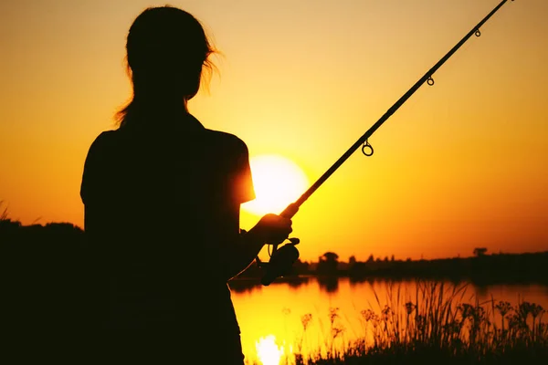 Silhueta de uma mulher de pesca na margem do rio ao pôr-do-sol — Fotografia de Stock