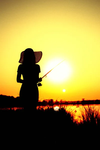 Silhouette della figura di awoman in un cappello con una canna da pesca sulla riva del fiume — Foto Stock