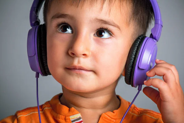 Studioporträt eines kleinen lustigen Jungen mit braunen Augen im Kopfhörer, der Musik auf grauem Hintergrund hört, Emotionen der Freude, Überraschung — Stockfoto