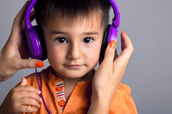 Studioporträt eines Jungen, dem Mutter oder Schwester Kopfhörer mit Musik auf grauem Hintergrund tragen — Stockfoto