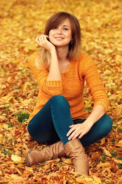 Portrait de mode d'automne d'une femme positive assise sur un feuillage jaune tombé — Photo